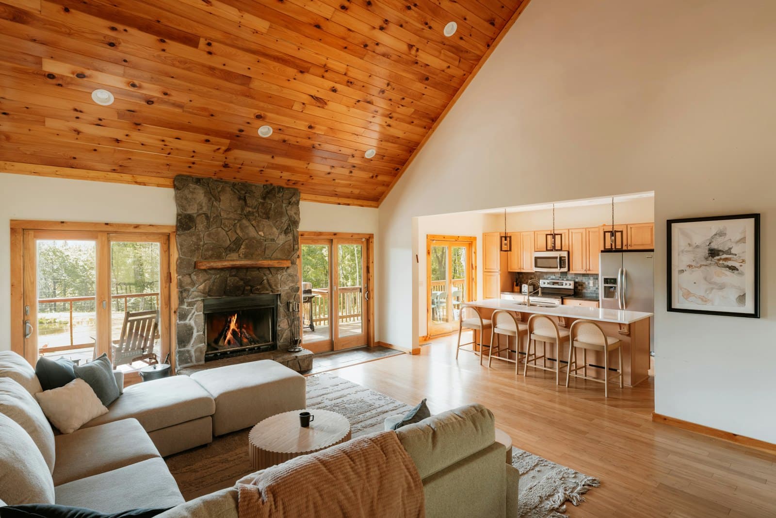 A bright living room with a stone fireplace and timber ceiling